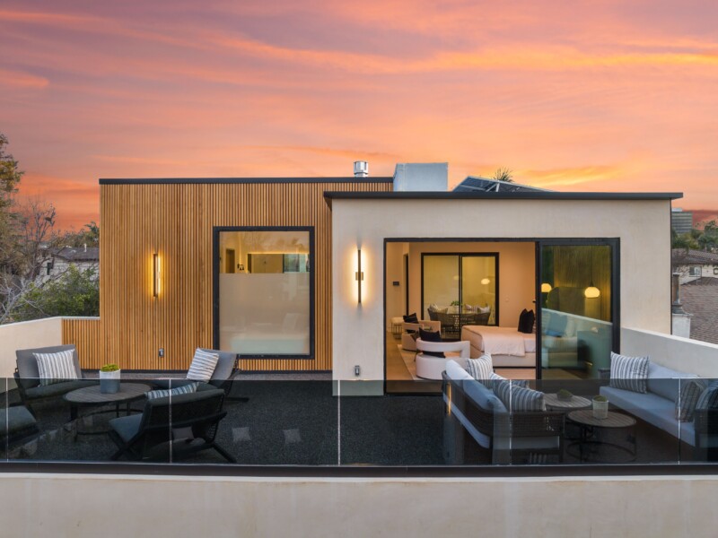 Modern rooftop patio with stylish furniture and sunset view, featuring a contemporary house with large windows and wooden accents.